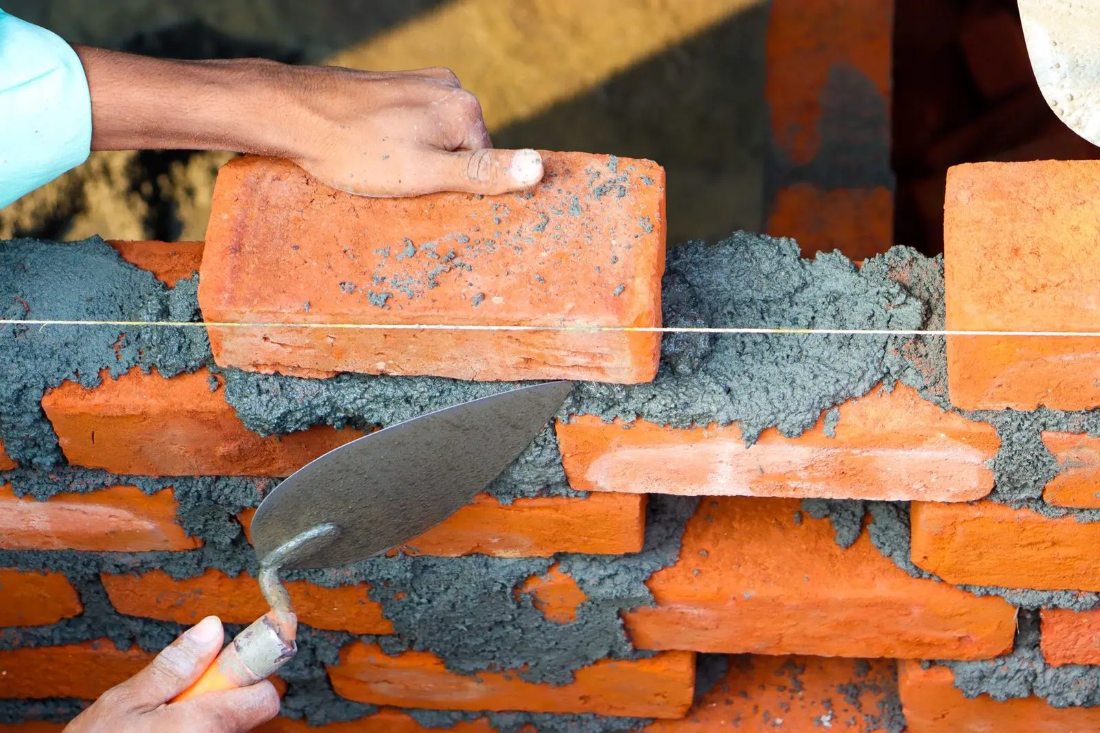 Mains posant des briques avec du mortier à la truelle