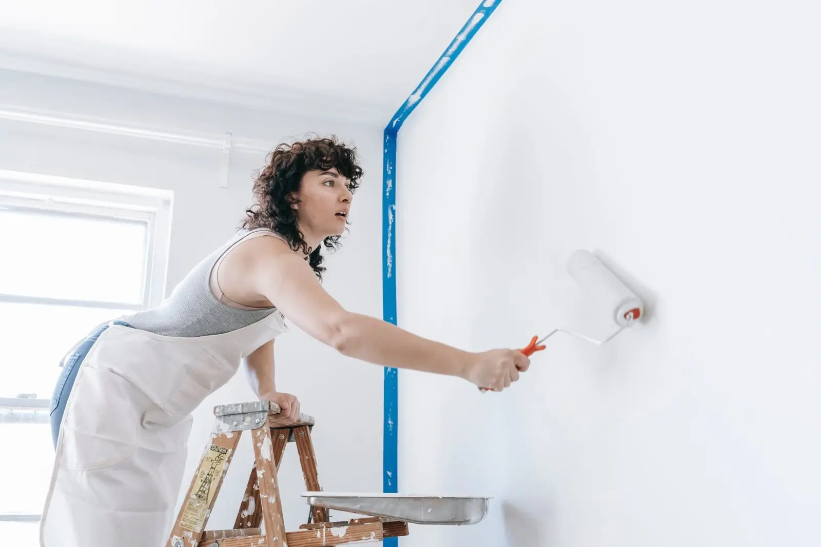 Peintre passant un rouleau sur un mur blanc avec des bandes de masquage