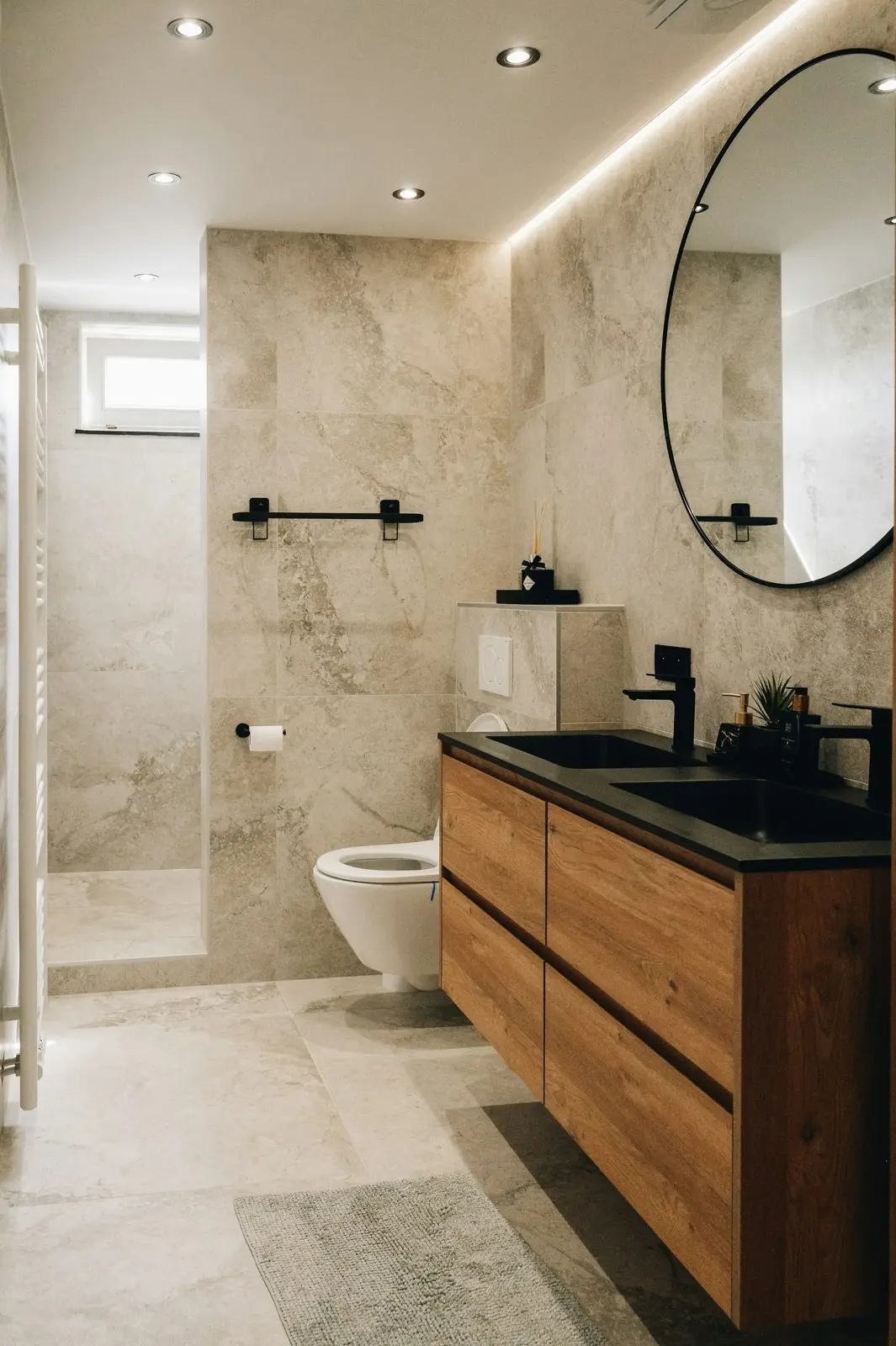 Salle de bain en pierre claire avec meuble en bois et miroir rond